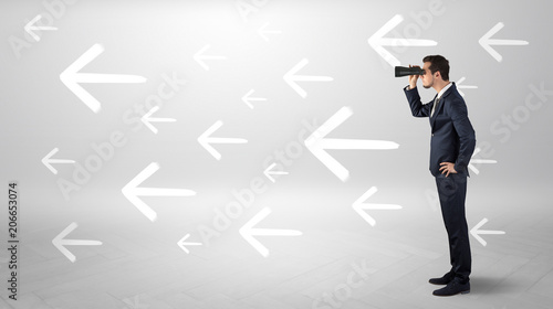 Young businessman standing and looking through binoculars with drawn arrows around  