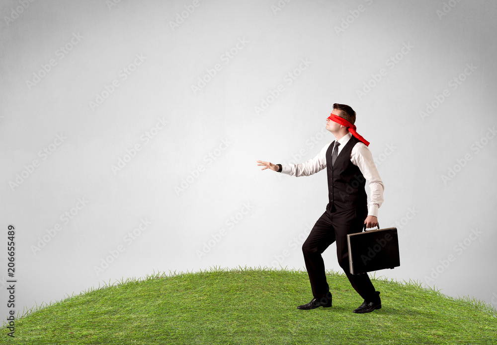 Young blindfolded businessman steps on a patch of grass Young blindfolded businessman steps on a patch of grass