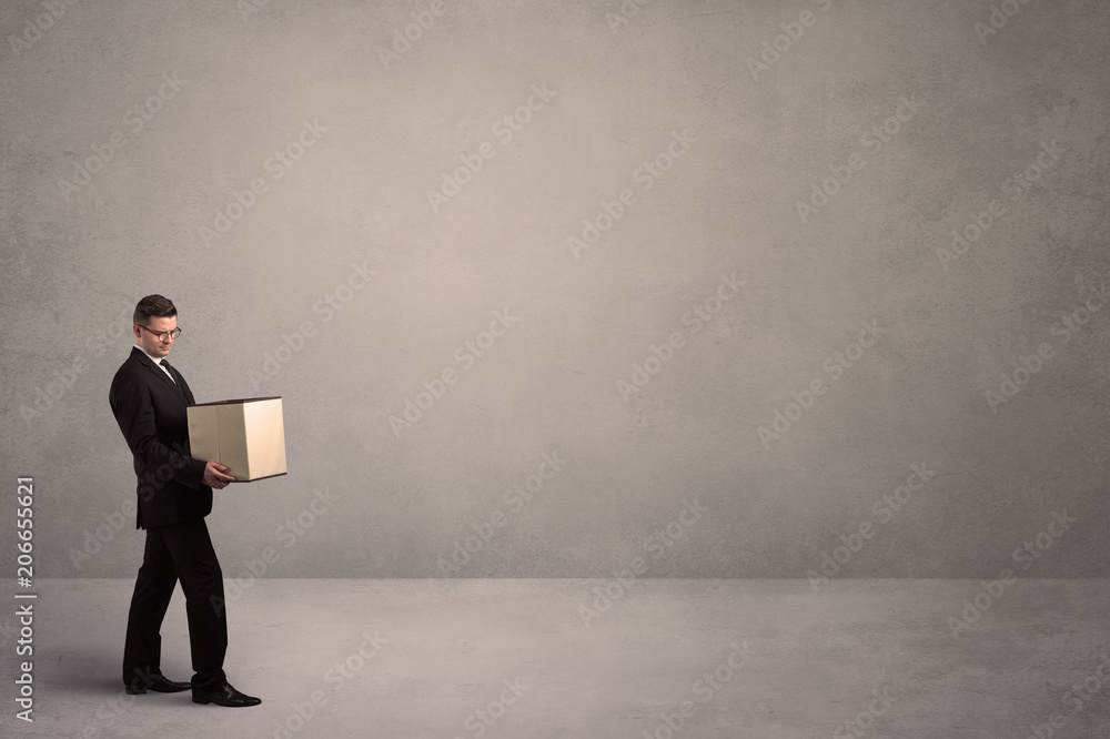 A well dressed young office worker holding an empty paper box with clear concrete wall background concept. A well dressed young office worker holding an empty paper box with clear concrete wall background concept.