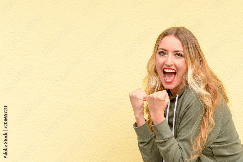 Excited blond woman cheering clenching her fists Excited blond woman cheering clenching her fists
