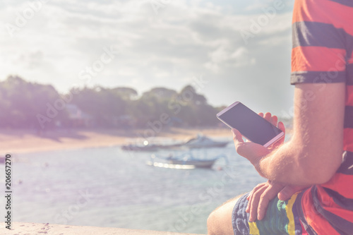 Man using cellphone on the ocean shore.