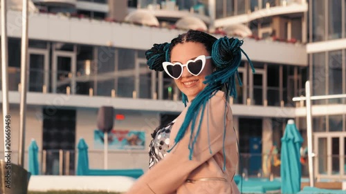 Portrait of beautiful girl with african kanekalon blue braids and heart shaped sunglasses on luxury resort hotel background. Afro hairstyle, freaky dyed hair. Hipster having fun. photo