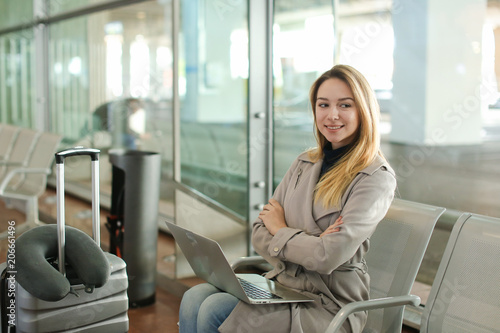 European girl sitting in waiting room with laptop and using social networks near valise. Concept of traveling and modern technology.