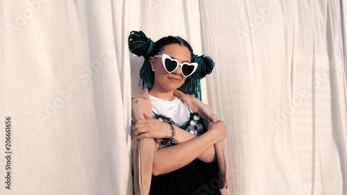 Portrait of beautiful girl with african kanekalon blue braids and heart shaped sunglasses on white cloth background. Afro hairstyle, freaky dyed hair. Hipster smiling to camera photo