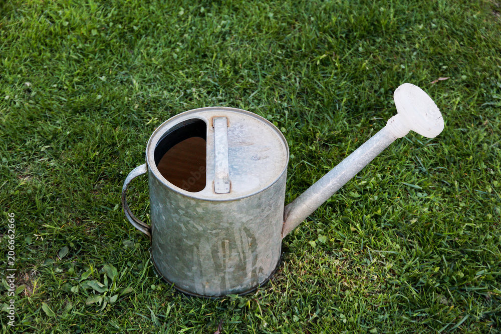 old metal watering can on the green grass old metal watering can on the green grass