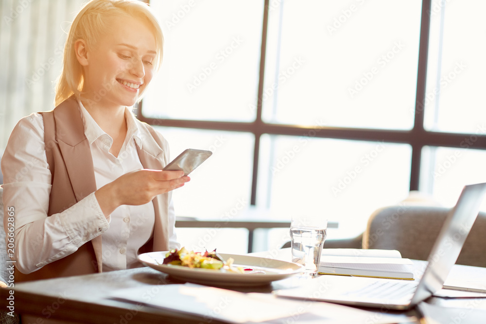 Young businesswoman texting in smartphone while having lunch in cafe Young businesswoman texting in smartphone while having lunch in cafe