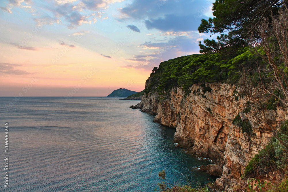 Cliff face with the sea and a beautiful sunset with birds flying in the sky - island of Kolocep in Croatia