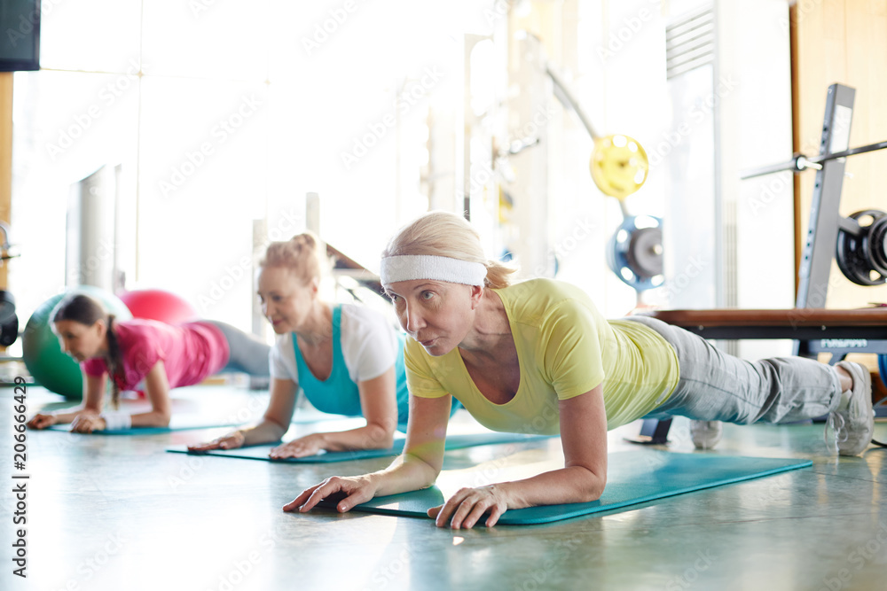 Row of active mature females doing planks on the floor in fitness center Row of active mature females doing planks on the floor in fitness center