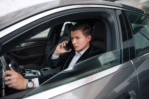 Drive calm! Side view portrait of the young handsome businessman looking on the left, while driving a car and talking the phone.