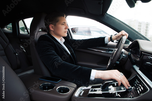 Do not hurry up! Handsome smart serious entrepreneur sitting on the driver's seat and carefully driving the automobile.