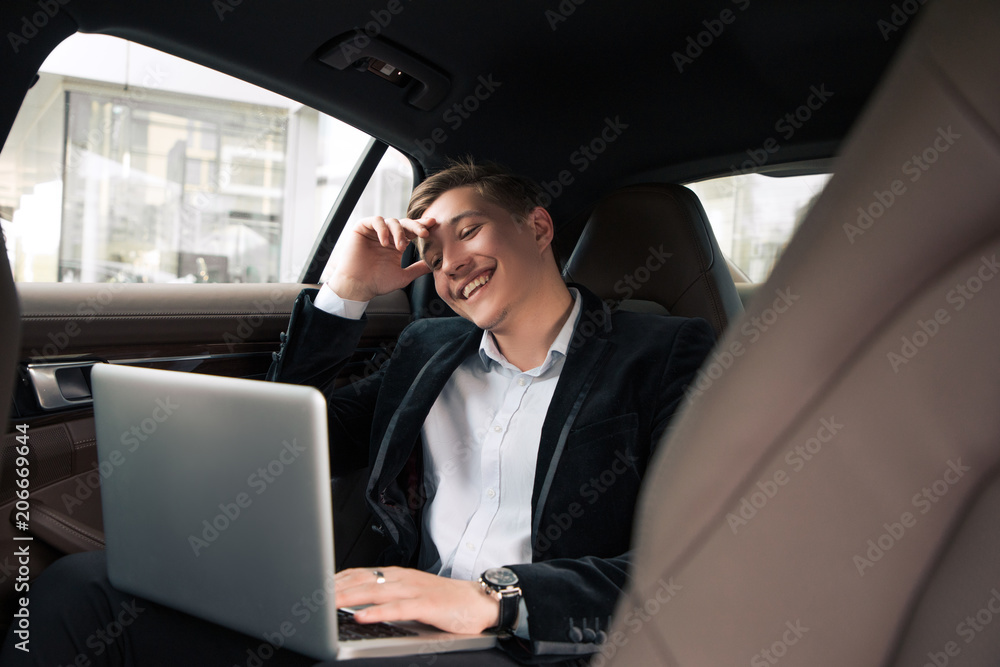 Be always cheerful and positive! Cheerful acknowledged young professional businessman sitting in the car and smiling, while working on the laptop. Be always cheerful and positive! Cheerful acknowledged young professional businessman sitting in the car and smiling, while working on the laptop.
