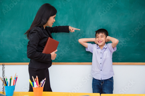 Valokuva Asian schoolboy clse ears by hands and smiles while teacher scold him in classro