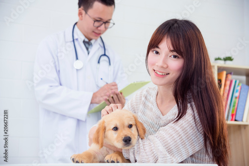 Asian young female owner posing with her puppy dog smiling to camera at the vet clinic