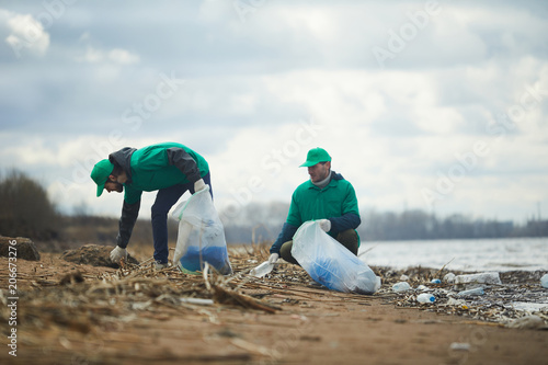 Ecology organization workers picking litter from dirty territory and utilizing it into special sacks photo