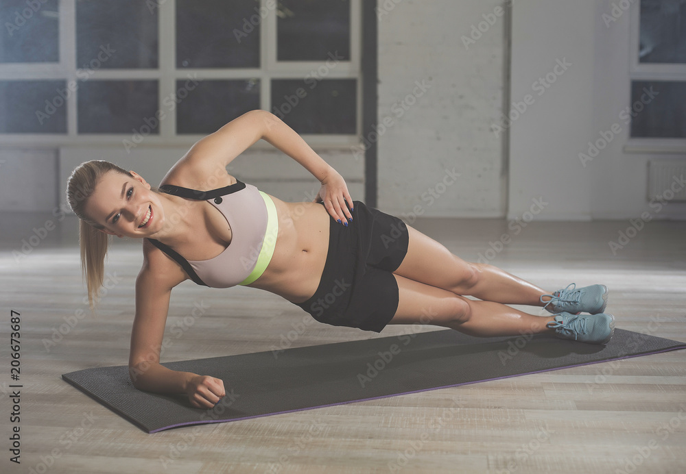 Full length portrait of attractive, smiling woman training on carrymat. She is leaning on elbow while holding her waist with left hand facing camera Full length portrait of attractive, smiling woman training on carrymat. She is leaning on elbow while holding her waist with left hand facing camera