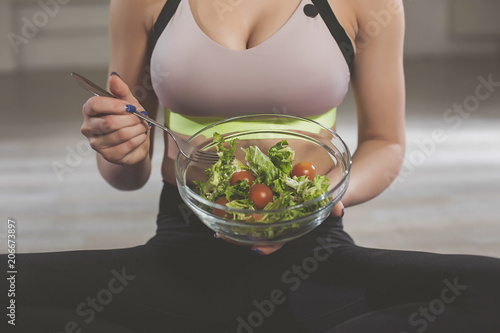 Close up of girl showing green salad mix with lettuce and ripe red tomatoes. Young female is sitting on floor preparing to eat