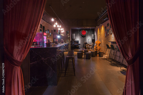 Modern jazz bar interior design, stage with black piano and cello, lamps above bar counter
