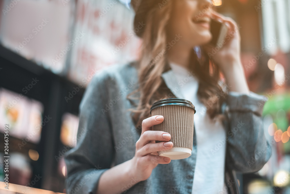 Low angle focus on woman hand holding cup of coffee. Cheerful girl is enjoying phone conversation Low angle focus on woman hand holding cup of coffee. Cheerful girl is enjoying phone conversation