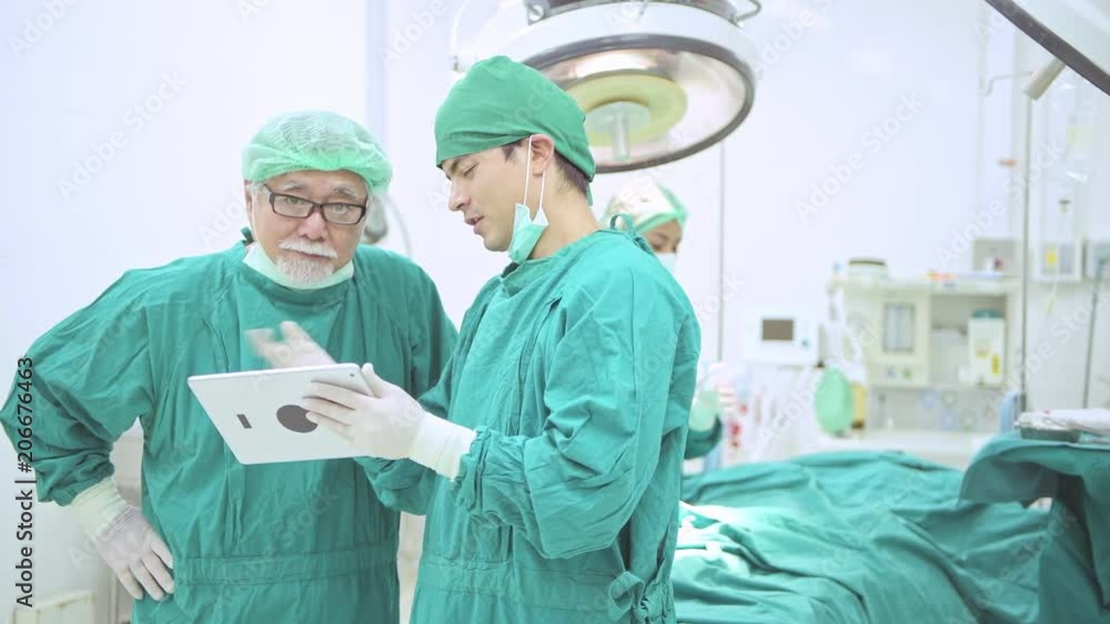 Surgery team looking at operation result in tablet. Happy young white male surgeon and his senior chinese male surgeon talking together looking at tablet after successful operation in theatre, dolly. Surgery team looking at operation result in tablet. Happy young white male surgeon and his senior chinese male surgeon talking together looking at tablet after successful operation in theatre, dolly.