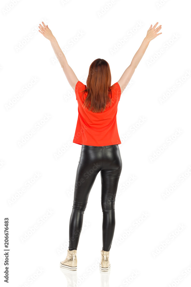 Woman In Leather Trousers And Orange Shirt Is Standing With Arms Raised. Rear View. Woman In Leather Trousers And Orange Shirt Is Standing With Arms Raised. Rear View.