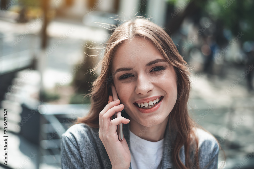 Portrait of joyful lady chatting on the smartphone. She is standing outdoors and looking happy Portrait of joyful lady chatting on the smartphone. She is standing outdoors and looking happy
