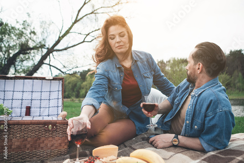 Relaxed loving couple is drinking wine in the nature. They are resting on blanket. Beautiful river is on background 