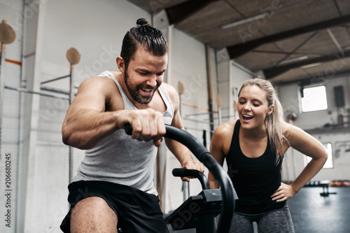 Smiling woman cheering on her gym partner riding a bike