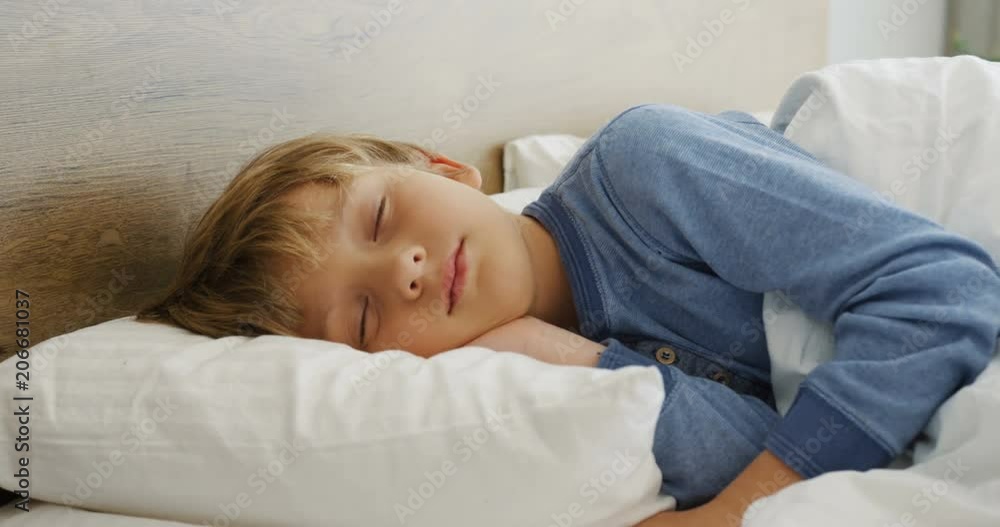 Portrait of the pretty little blonde boy dreaming in a cozy bed in the morning. Indoor Portrait of the pretty little blonde boy dreaming in a cozy bed in the morning. Indoor