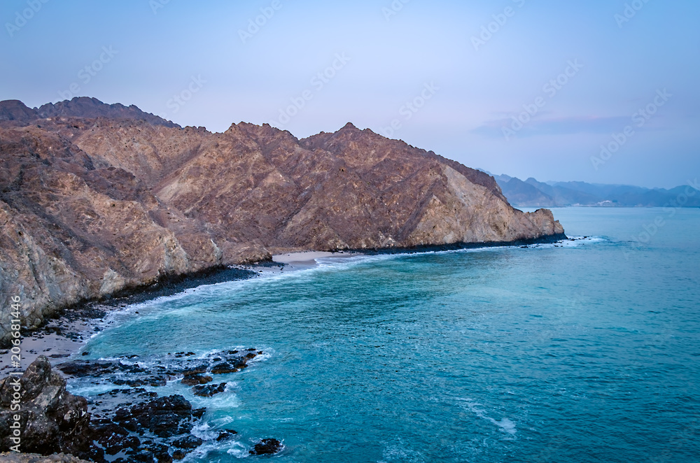 Muscat Beach Landscape. Beautiful bird's eye view of barren, pointy mountains and turquoise sea water in Oman.