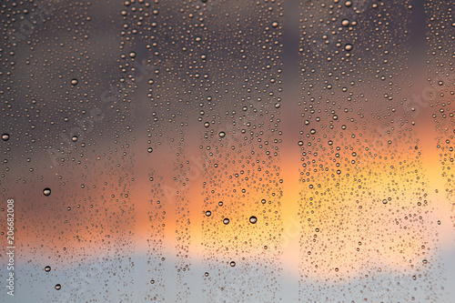 texture of rain drops on dirty window glass over blur and cloudy sunset sky background 