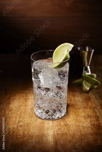 Spotlight on a crystal glasses full of the Gin and tonic cocktail, with a lime garnish, shot on a antique wooden table top. photo