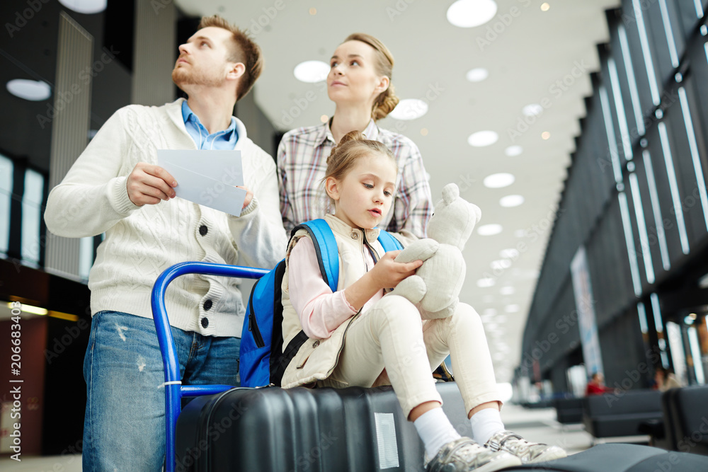 Young couple looking at tableau while moving towards entrance to platform with their daughter sitting on baggage
