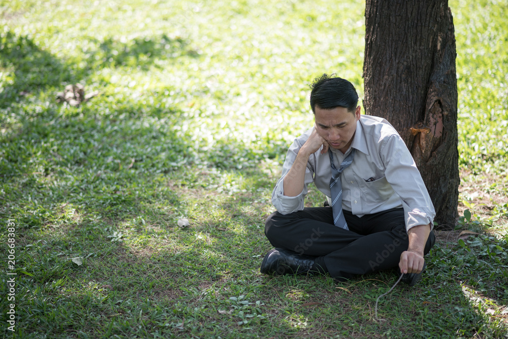Business man failing and serious under tree in the park. He is stressed with work Unsuccessful disappointed in project Business man failing and serious under tree in the park. He is stressed with work Unsuccessful disappointed in project