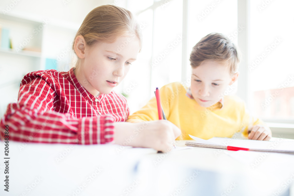 Two schoolkids with highlighters drawing together while carrying out task at lesson Two schoolkids with highlighters drawing together while carrying out task at lesson