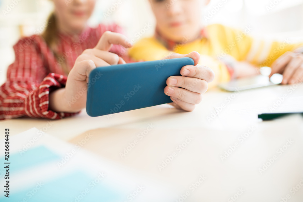 Two modern schoolmates playing in smartphone over desk during break between lessons Two modern schoolmates playing in smartphone over desk during break between lessons