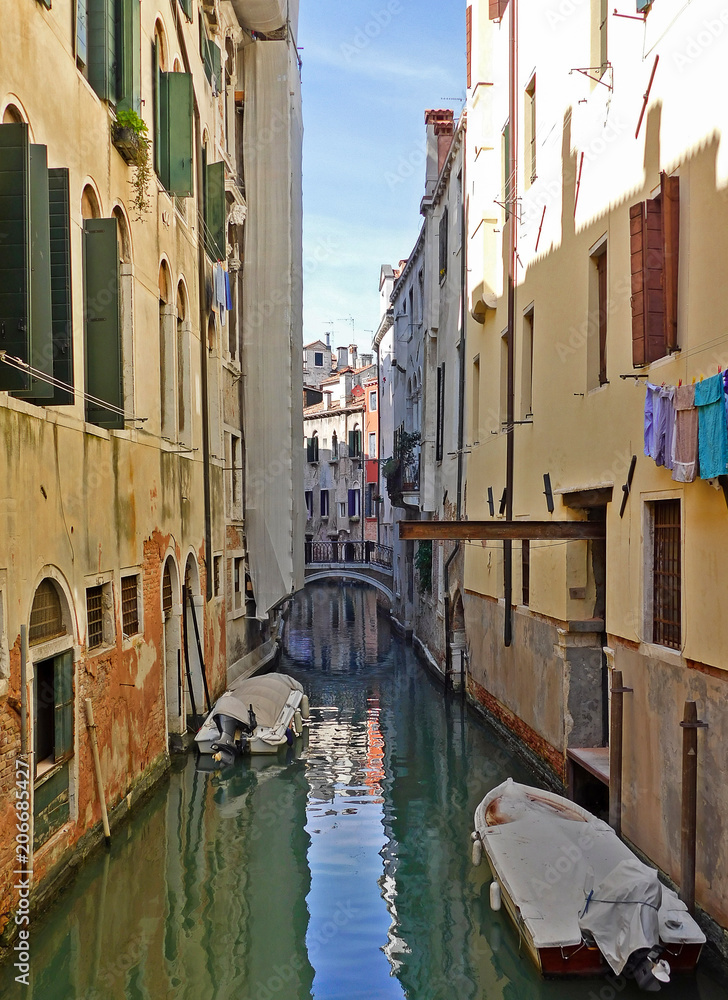 View of a typical street in Venice, Italy. Green water canal between houses. Boats at the door