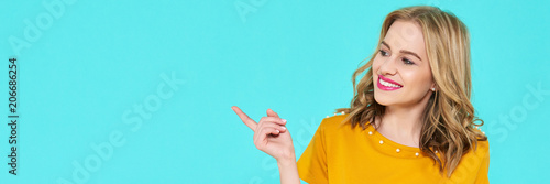 Obraz na plátně Trendy attractive young woman wearing mustard color summer dress posing over pastel blue background