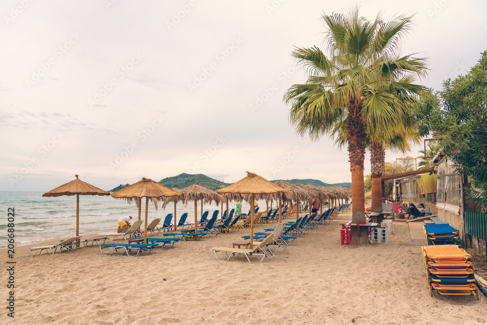 Alikanas, Zakynthos Island, Greece – September 28, 2017: Sunbeds, umbrellas and palms on the Alikanas beach, Zakynthos Island, Greece. Alikanas, Zakynthos Island, Greece – September 28, 2017: Sunbeds, umbrellas and palms on the Alikanas beach, Zakynthos Island, Greece.