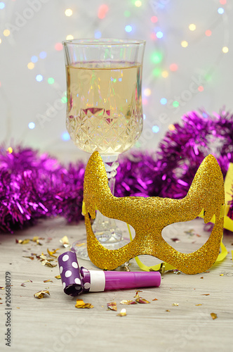 A glass of champagne displayed with a mask, party blower and tinsel