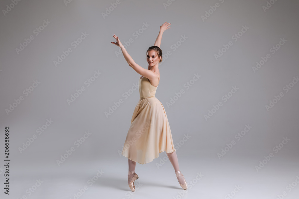 The reflection of a dancing lady! Young attractive gentle ballerina dancing and posing on the isolated grey background indoors.