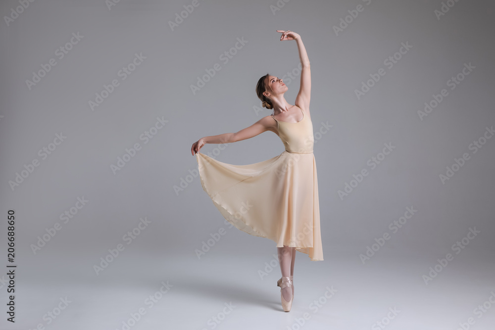 Fototapeta premium Timeless interpretation of life! Full length photo of the young beautiful ballerina fulfilling movements on the light background.