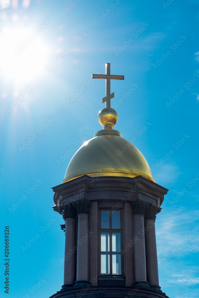 Gold dome and a cross on a background of blue sky and bright sunlight