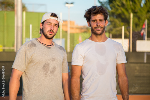 Two tennis players standing on tennis court during break and laughing. 