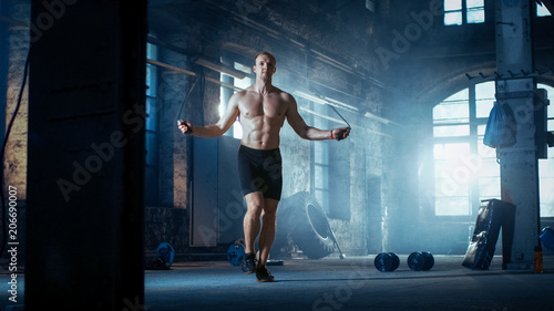 Muscular Fit Man Exercises with Jump / Skipping Rope in a Deserted Factory Hardcore Gym. He's Sweaty from His Cross Fitness Exhausting Training.