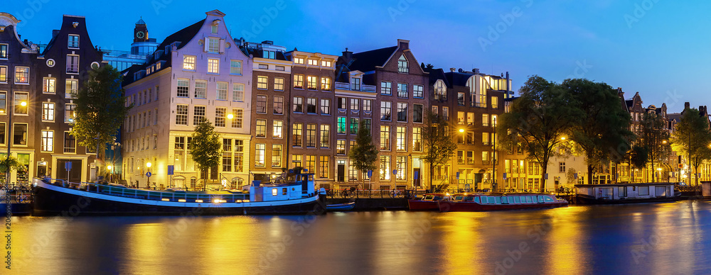Night panoramic city view of Amsterdam canal, typical dutch houses and boats, Holland, Netherlands.
