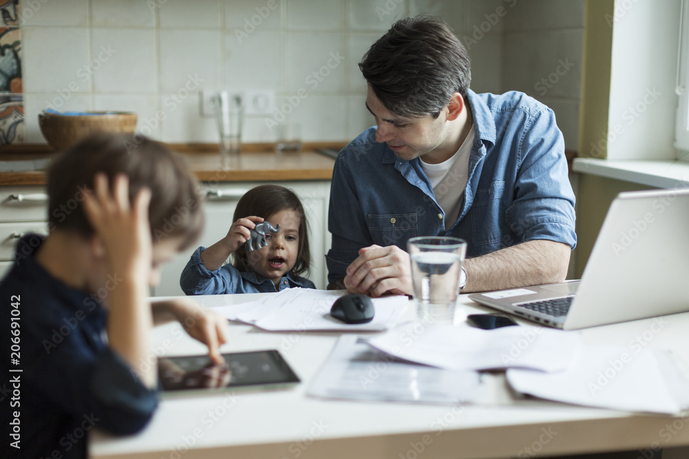 Young father working at home and looking after son and daughter Young father working at home and looking after son and daughter