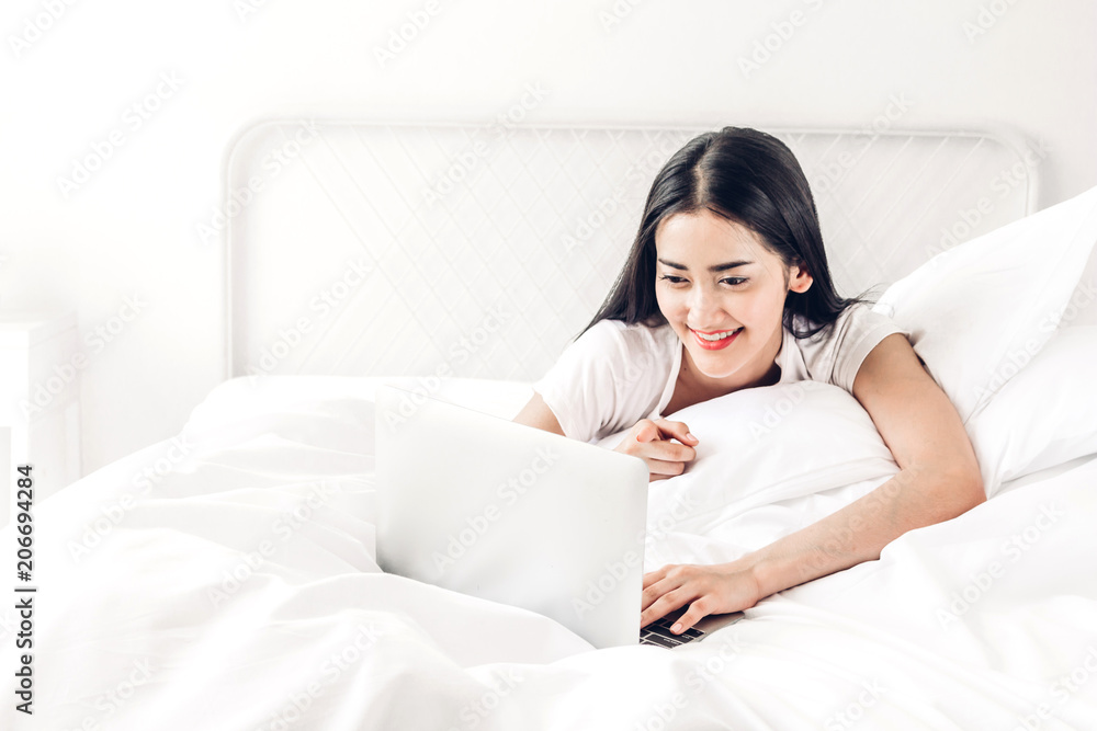 Happy woman relaxing and using digital laptop computer on the bed at home.woman checking social apps and working with smartphone Happy woman relaxing and using digital laptop computer on the bed at home.woman checking social apps and working with smartphone