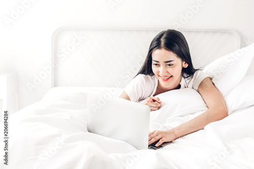 Happy woman relaxing and using digital laptop computer on the bed at home.woman checking social apps and working with smartphone