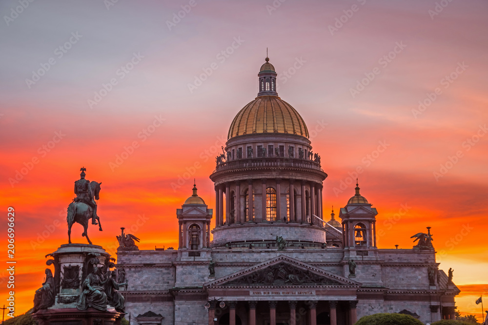 St. Isaac's Cathedral in the square, in St. Peterburg in the evening on a bright orange sunset sky, left monument-rider on horse Nikolai.