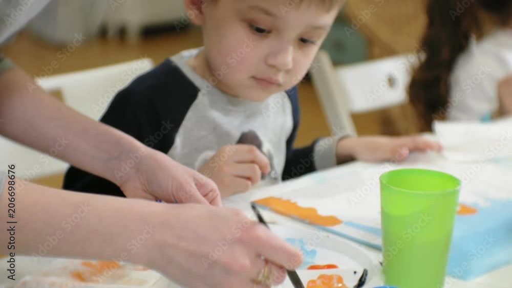 Children boys and girls sitting together around the table in classroom and drawing. With them is their young and beautiful teacher. Children boys and girls sitting together around the table in classroom and drawing. With them is their young and beautiful teacher.